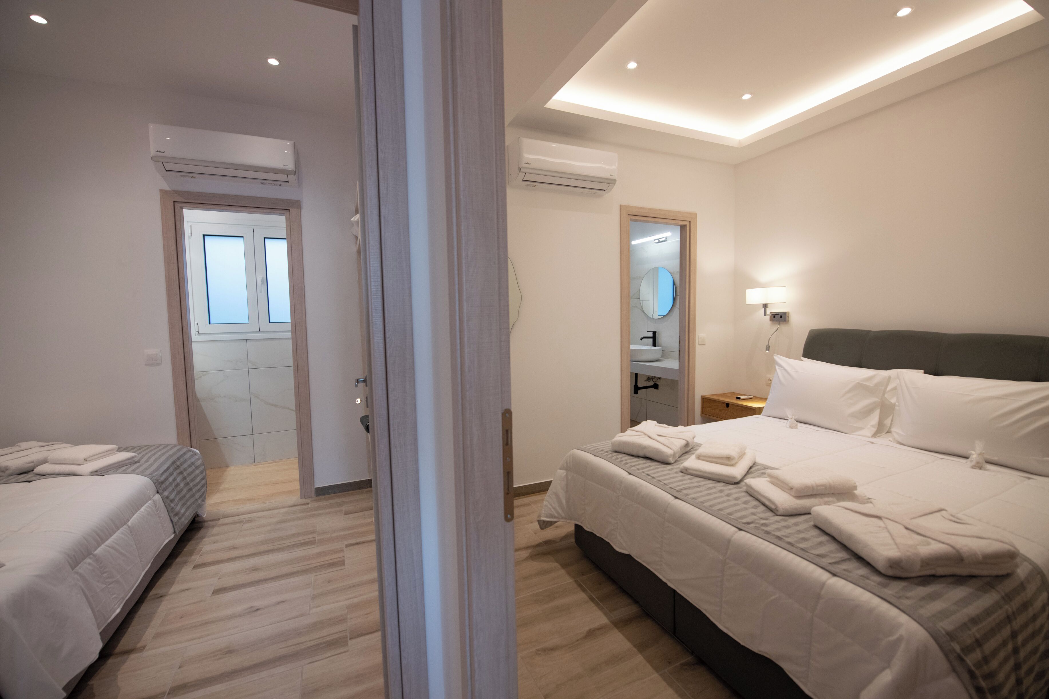 Moderni hotellihuone, jossa on kaksi sänkyä, kylpyhuone peilillä ja pesualtaalla sekä ilmastointilaite.