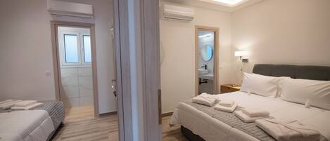 Moderni hotellihuone, jossa on kaksi sänkyä, kylpyhuone peilillä ja pesualtaalla sekä ilmastointilaite.