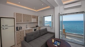 Ein kompakter, moderner Raum mit Küchenzeile, einem grauen Sofa, einem kleinen Tisch und einem großen Fenster mit Meerblick.