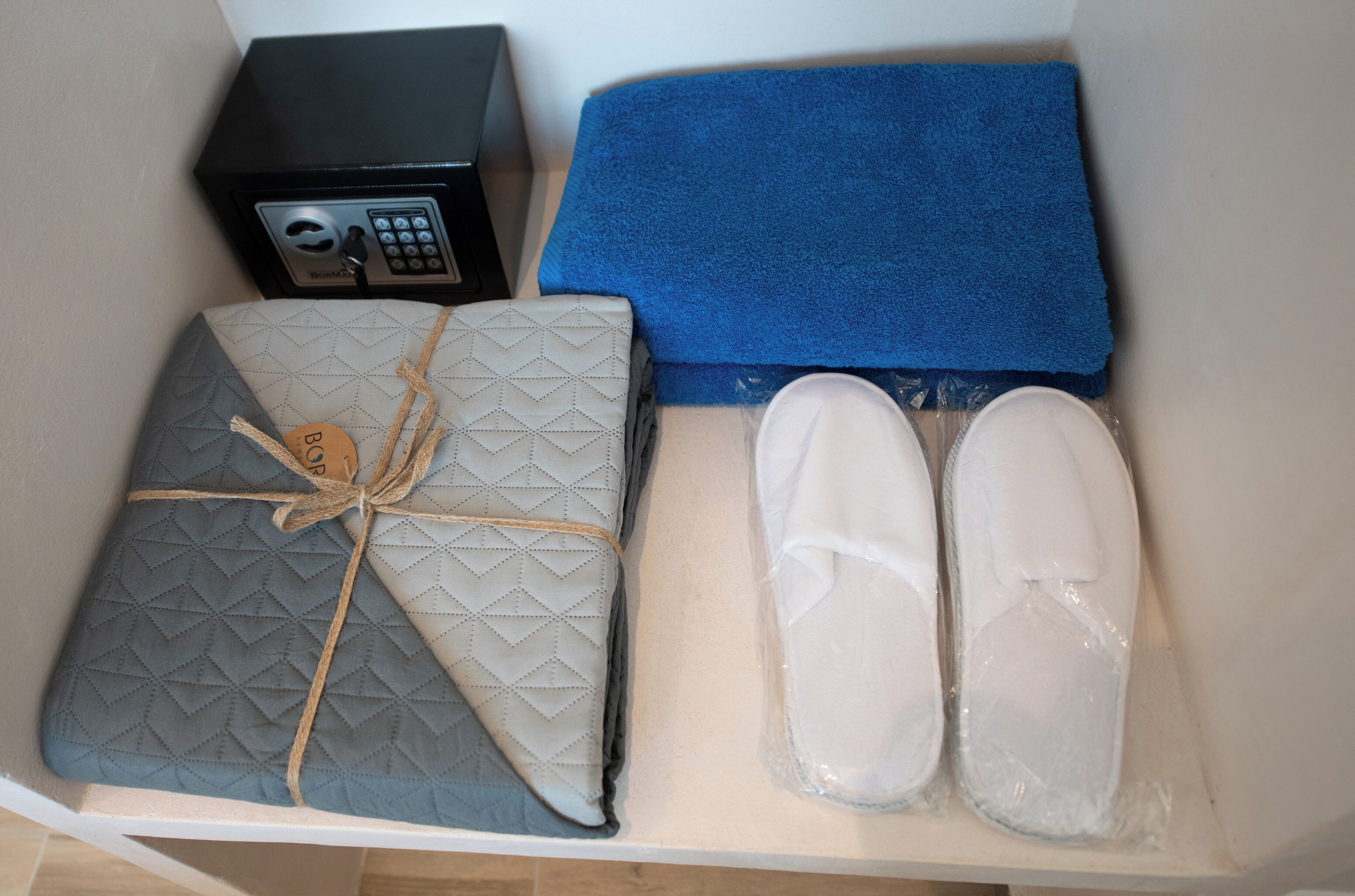 A box containing a quilted pillow, a blue towel, and a pair of slippers.