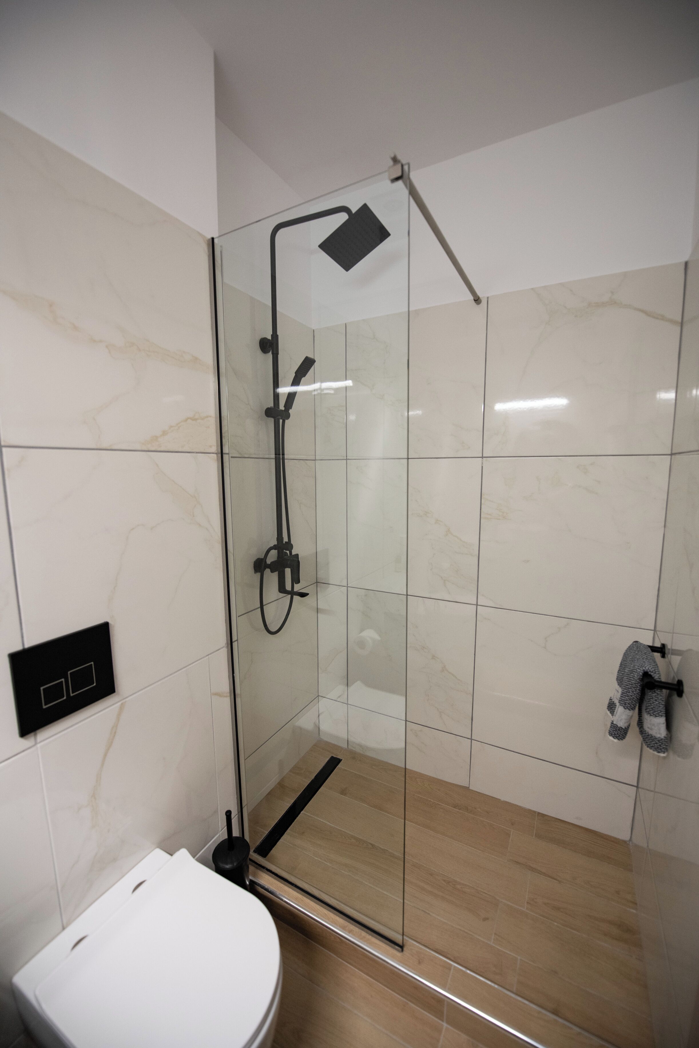 A modern bathroom with a glass-enclosed shower, a white toilet, and a marble-tiled wall.