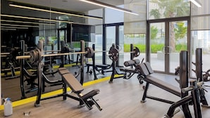 Un gimnasio moderno con equipo de levantamiento de pesas, espejos amplios y vistas al exterior con vegetación.