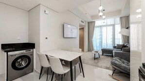 Una sala de estar moderna con un sofá, una mesa de comedor con sillas, una lavadora y un televisor montado en la pared.