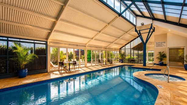 An indoor swimming pool with clear water, a sunroof, and a pool safety sign. - Abby's Beach Villa (Broadwater)