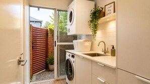 A compact laundry room with a washing machine, a sink, and a small shelf with a plant. - Abby's Beach Villa (Broadwater)