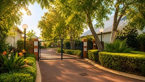 A gated entrance with a paved driveway, surrounded by well-maintained hedges and trees. - Abby's Beach Villa (Broadwater)