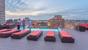 Un área de piscina en la azotea con sillones de descanso y vistas a la ciudad.