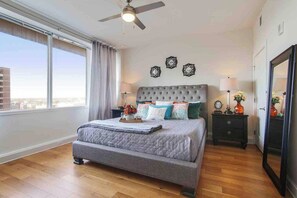 A bedroom with a large bed, a ceiling fan, a nightstand with a lamp, and a mirror. - Charming Condos in NOLA (New Orleans)
