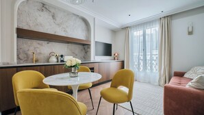 A modern hotel room with a marble accent wall, a kitchen area, a dining table with yellow chairs, and a red sofa. - Nestay Les Halles (Paris)