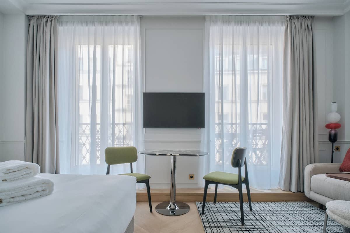 A hotel room with a bed, two chairs, a small table, a TV, and a sofa.