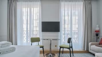Habitació d'hotel amb un llit, dues cadires, una taula petita, un televisor i un sofà.