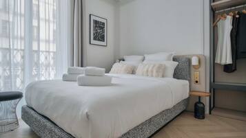 Ein modernes Schlafzimmer mit einem großen Bett, einem Nachttisch, einem kleinen Hocker und einem Kleiderschrank.