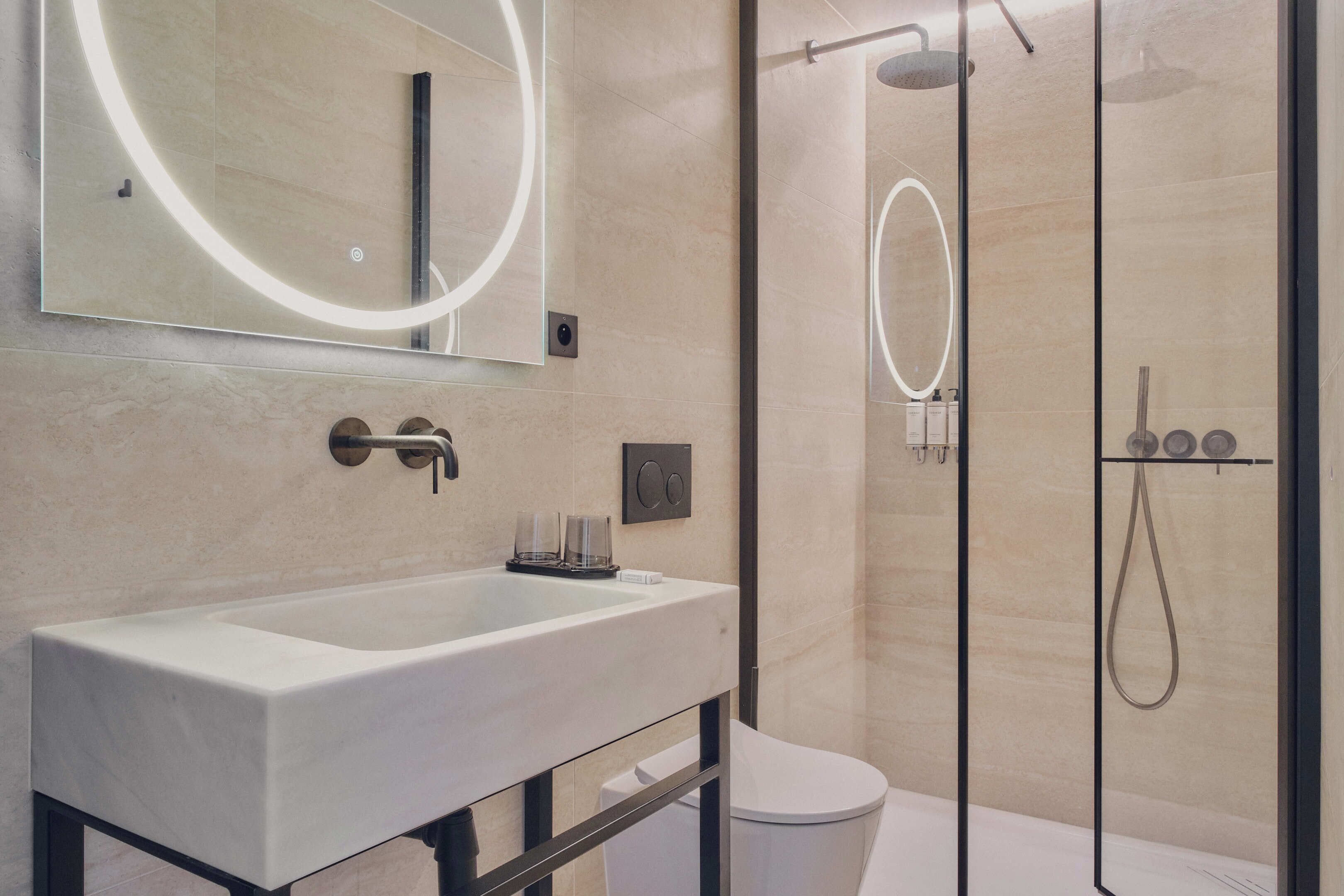 A modern bathroom with a large mirror, a rectangular sink, a toilet, and a glass-enclosed shower area.