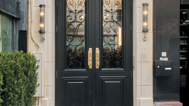 A black double door with ornate metalwork, a small plaque above, and two wall-mounted lights on either side. - Nestay Les Halles (Paris)