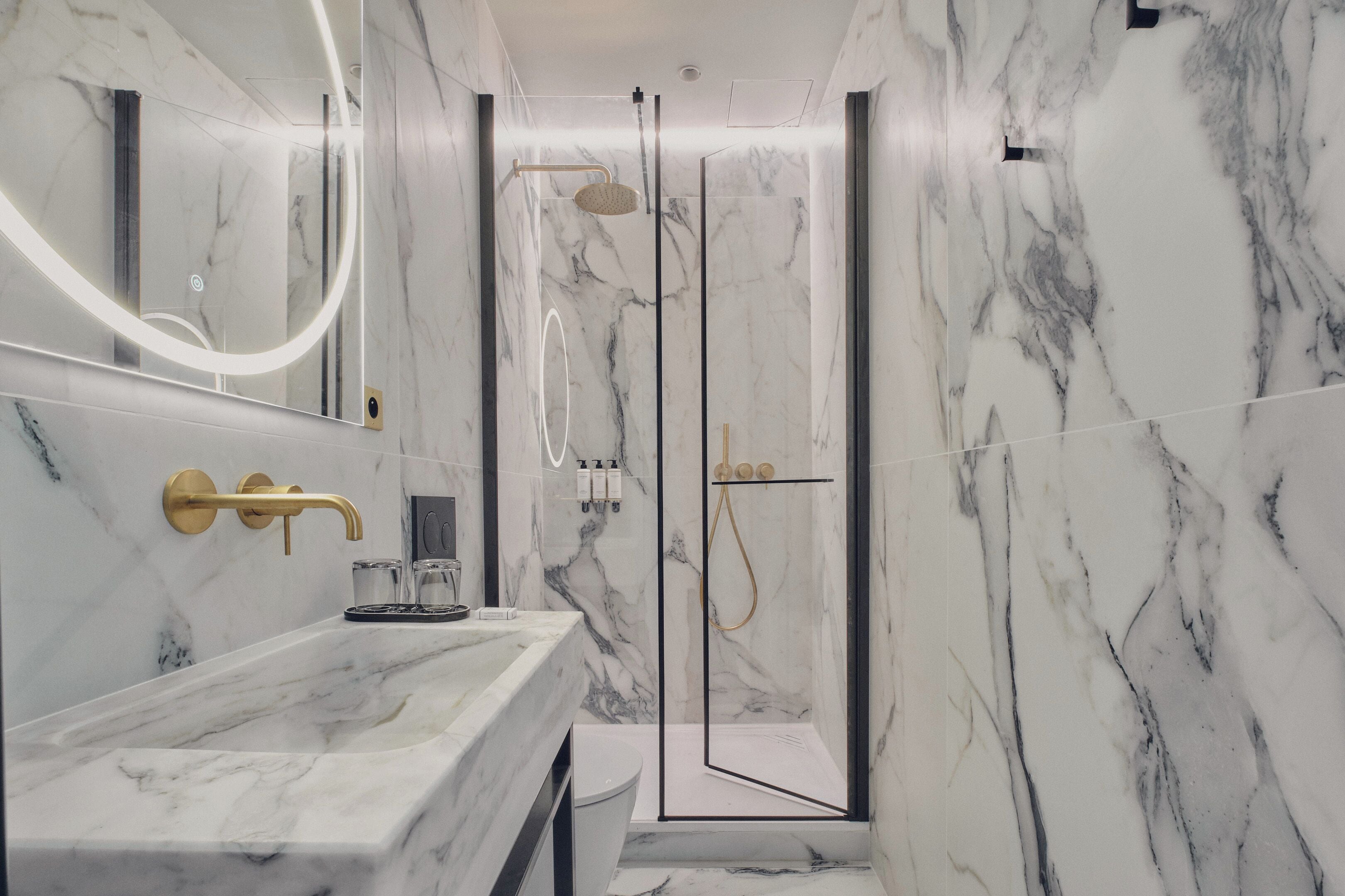 Une salle de bain moderne avec un lavabo en marbre, des robinetteries dorées et une douche à parois de verre.