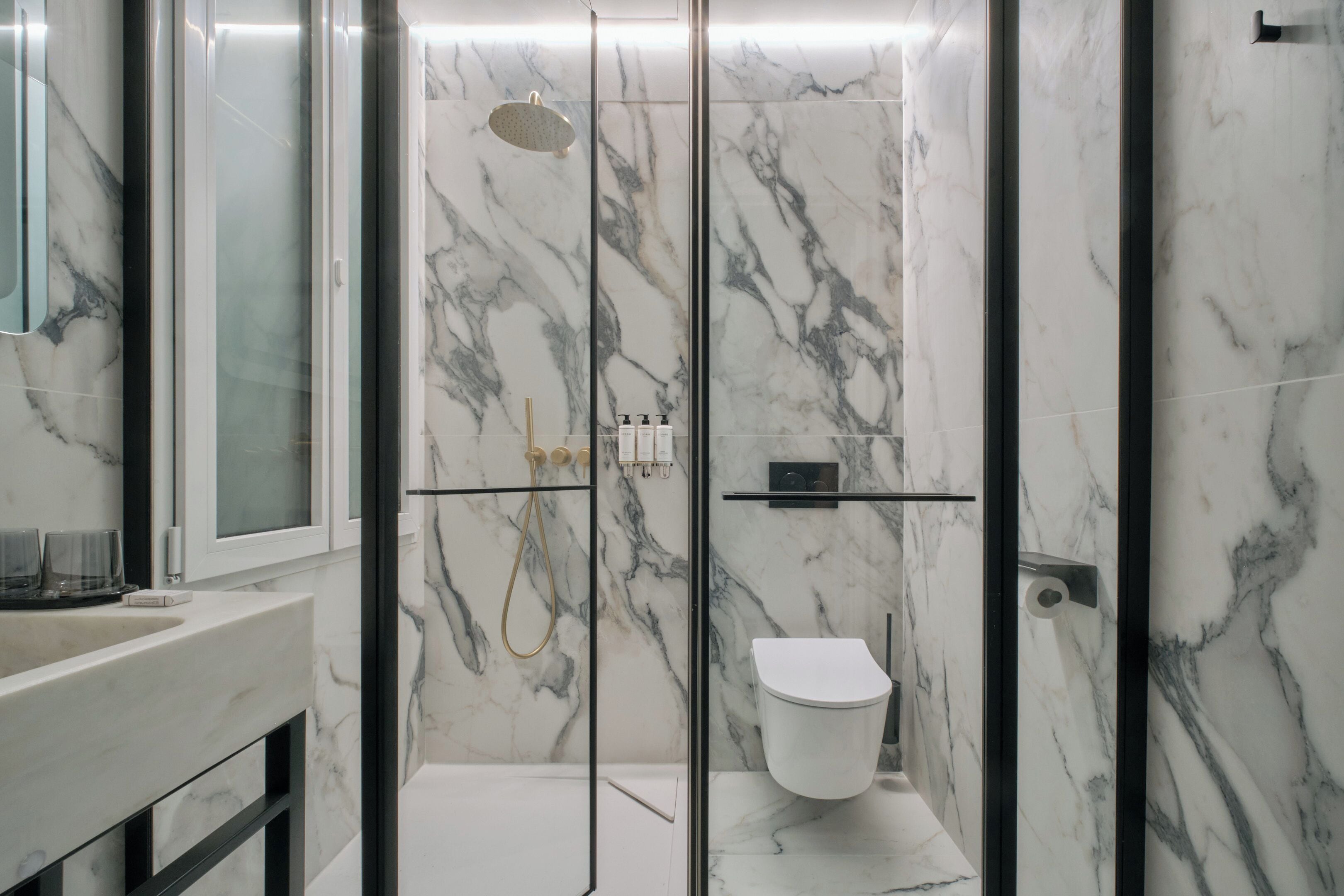 A modern bathroom with a glass-enclosed shower, a white toilet, and marble walls.