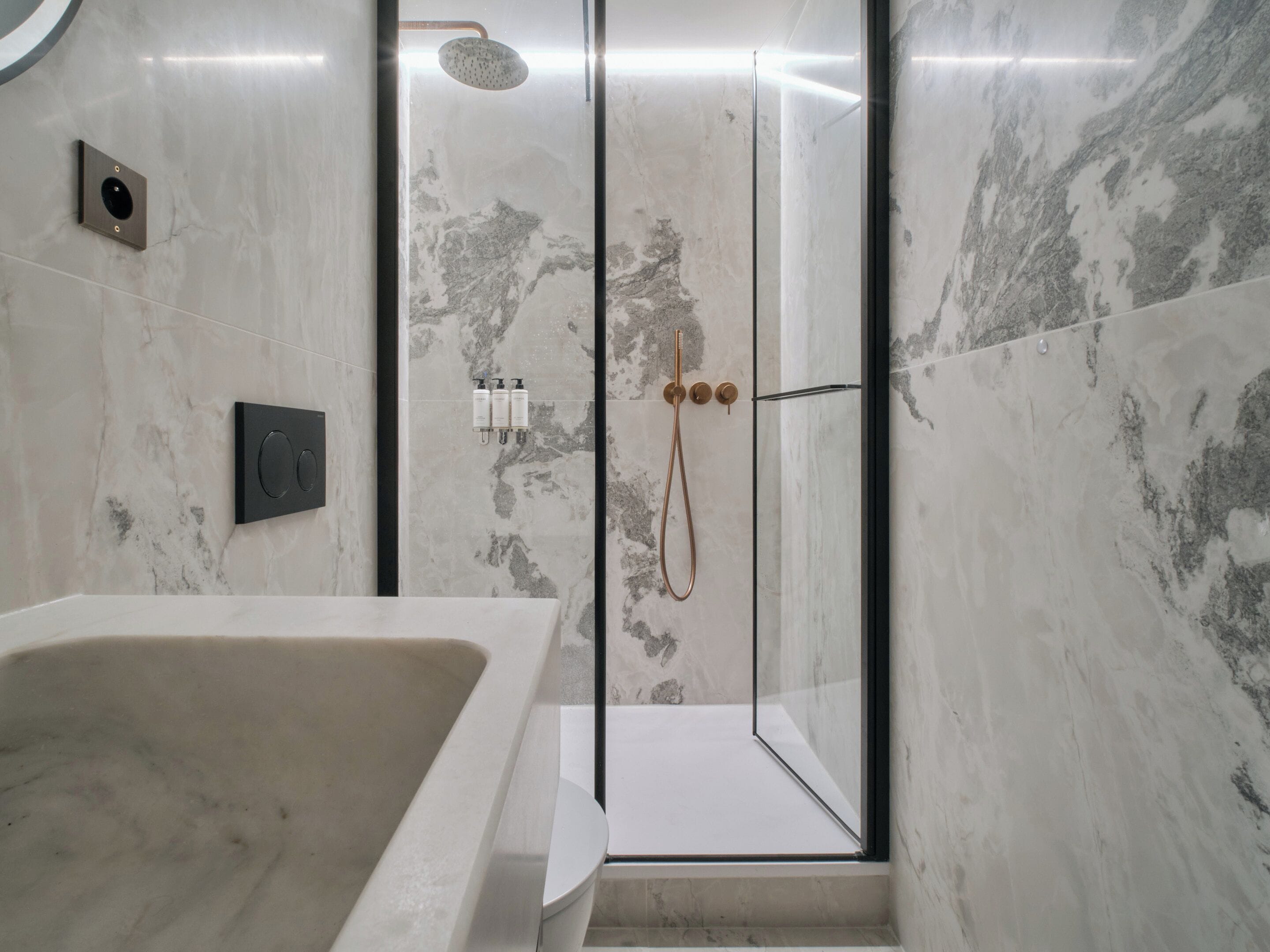 A modern bathroom with a freestanding bathtub, a glass-enclosed shower, and marble walls.