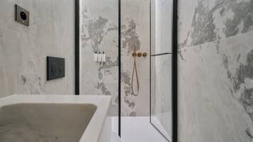 Un baño moderno con una bañera independiente, ducha con mampara de vidrio y paredes de mármol.