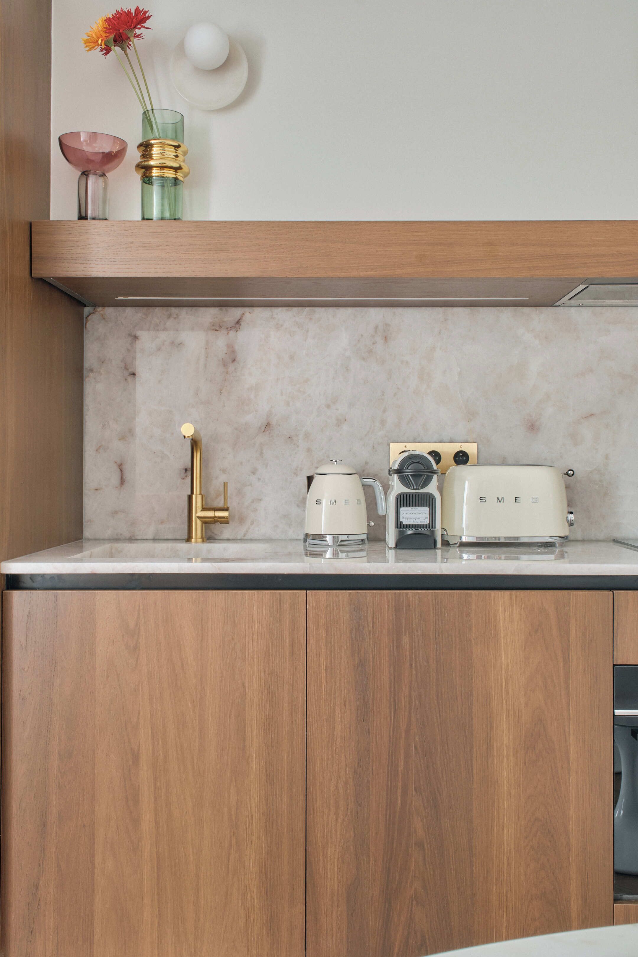 A kitchen with a marble countertop, wooden cabinets, a gold faucet, a vintage Sames coffee maker, a vintage Sames toaster, and a pink bowl.