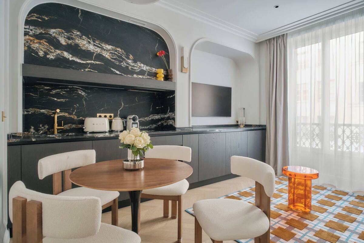 A modern kitchen with a marble backsplash, a round wooden table, and white chairs.