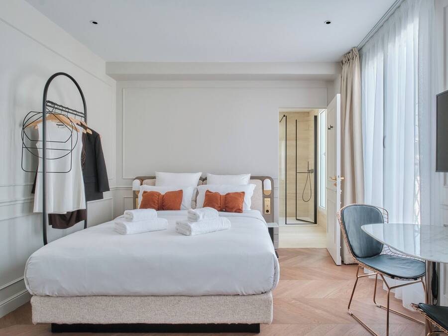 A neatly arranged hotel room with a bed, a chair, a table, and a TV.