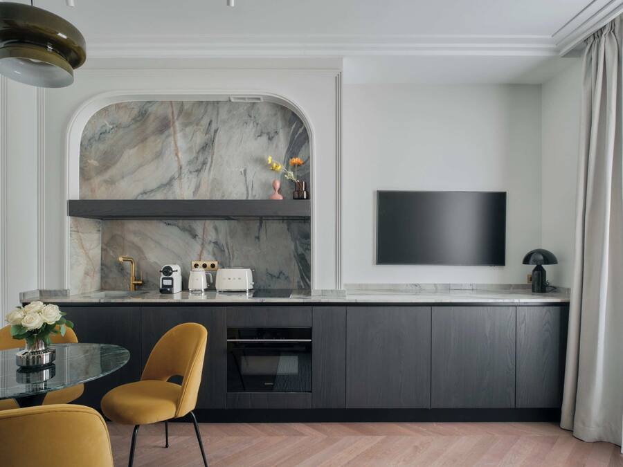 A modern kitchen with a marble backsplash, built-in oven, and a flat-screen TV mounted on the wall.