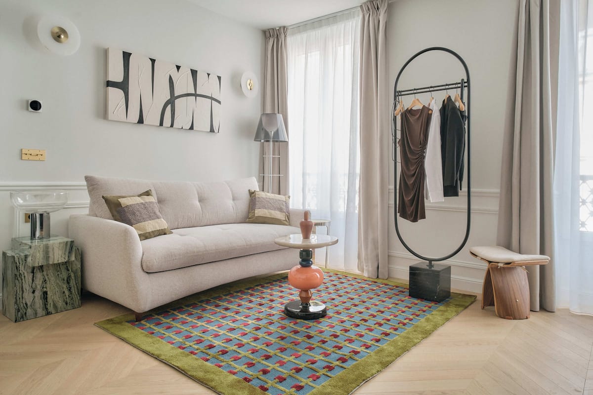 A modern living room with a sofa, a coffee table, a lamp, a hanging chair, and a clothing rack.