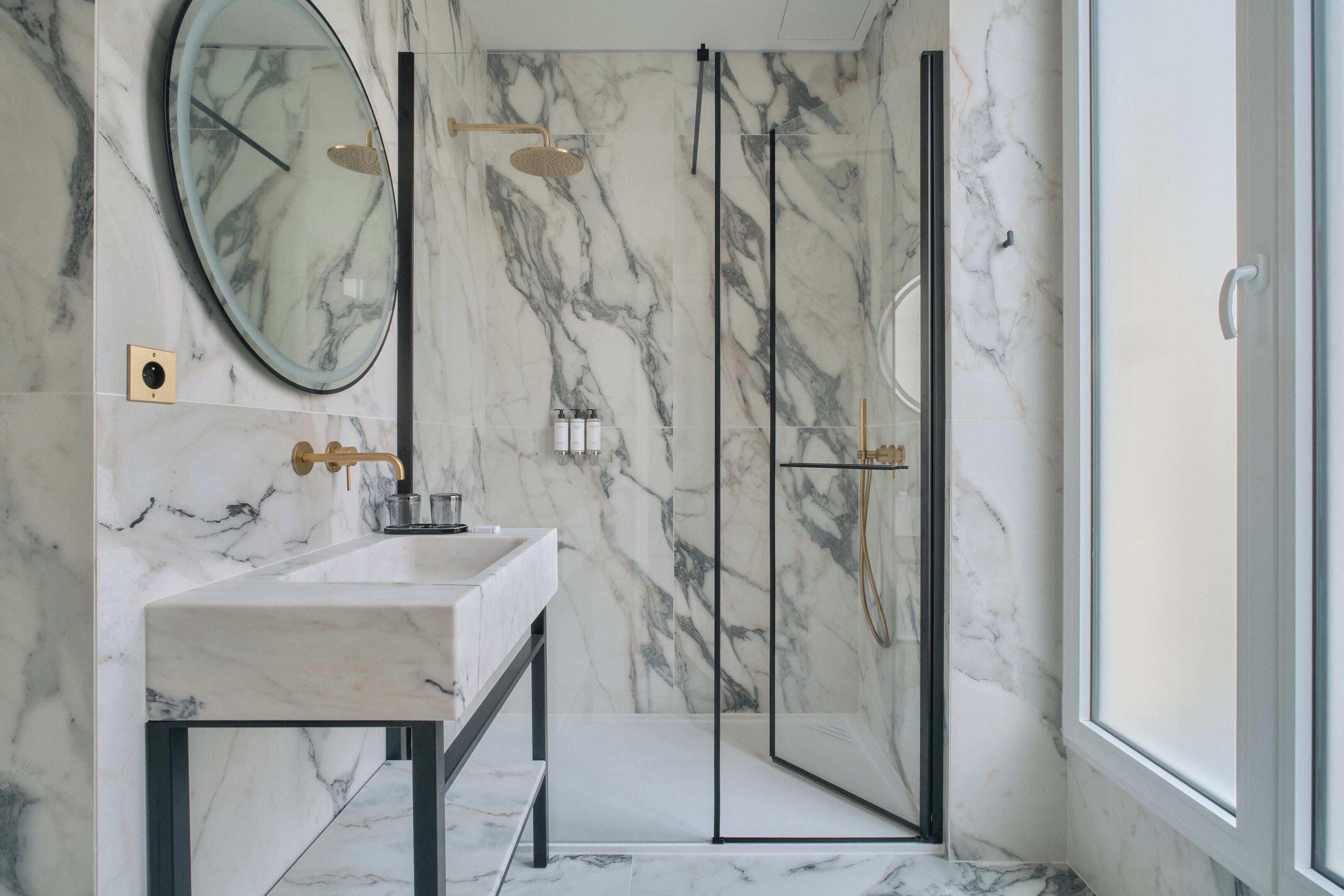 A bathroom with a marble wall, a sink, a mirror, and a glass-enclosed shower.