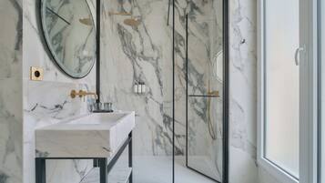 A bathroom with a marble wall, a sink, a mirror, and a glass-enclosed shower.