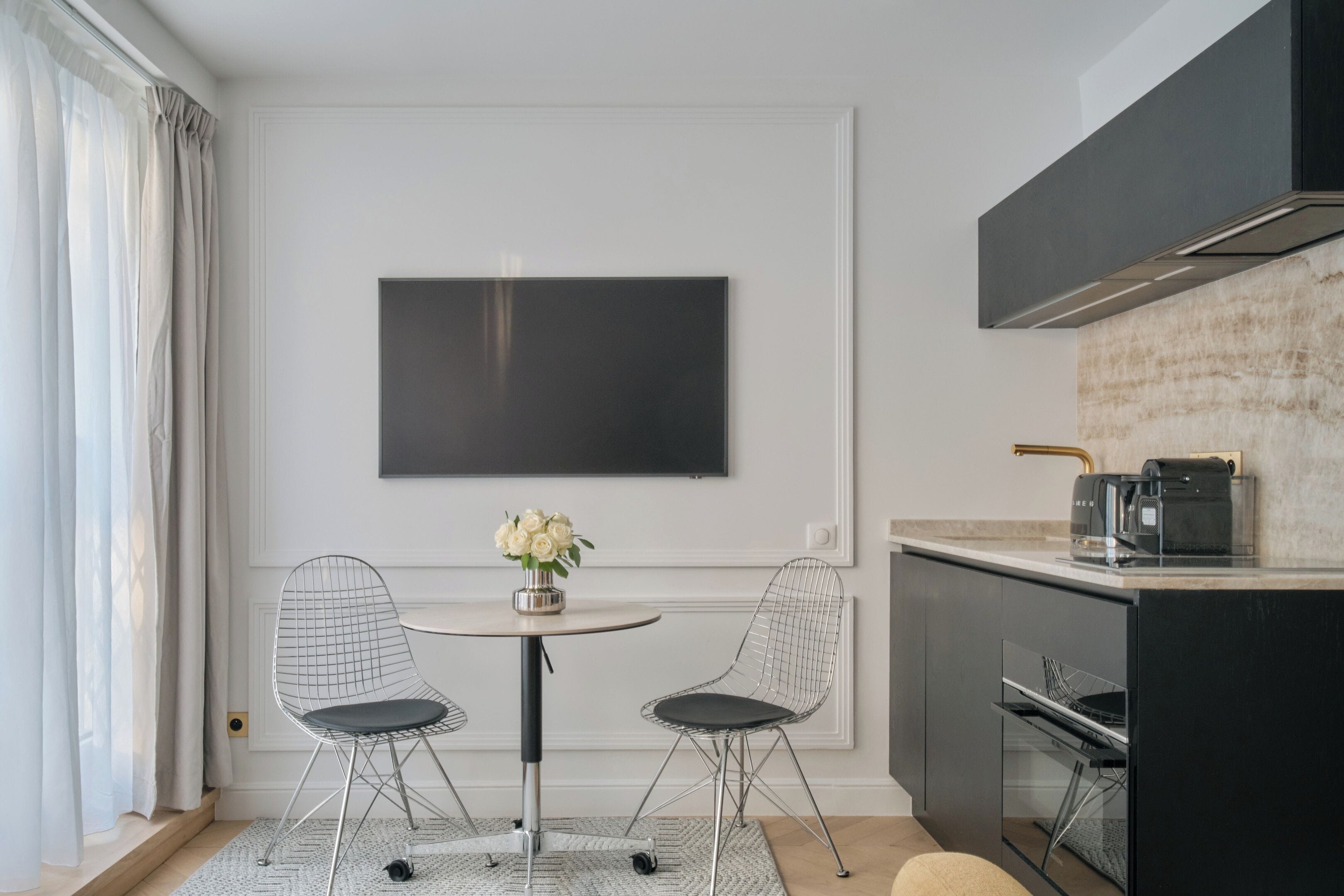 A modern kitchen with a dining area, a flat-screen TV, and a coffee machine.