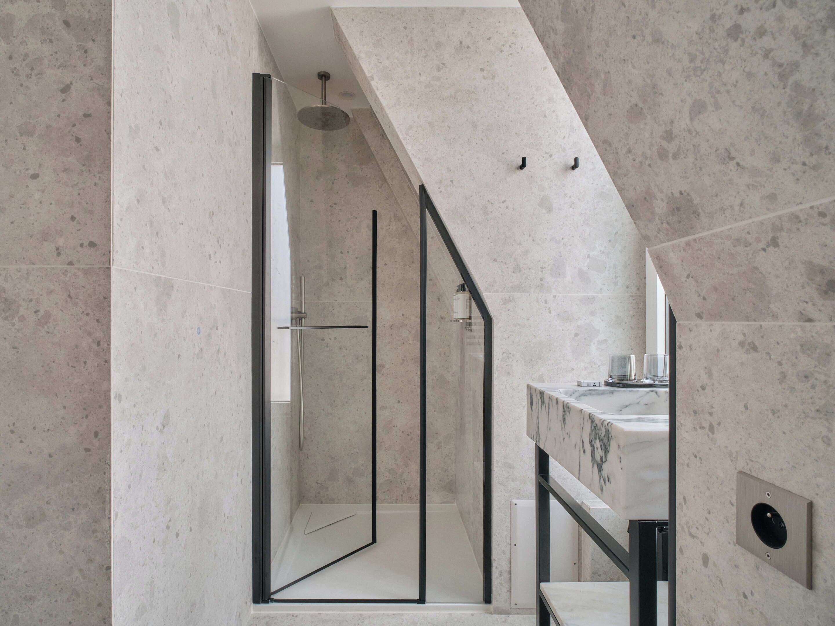 Un baño moderno con ducha, un lavamanos de mármol y una escalera de cristal.