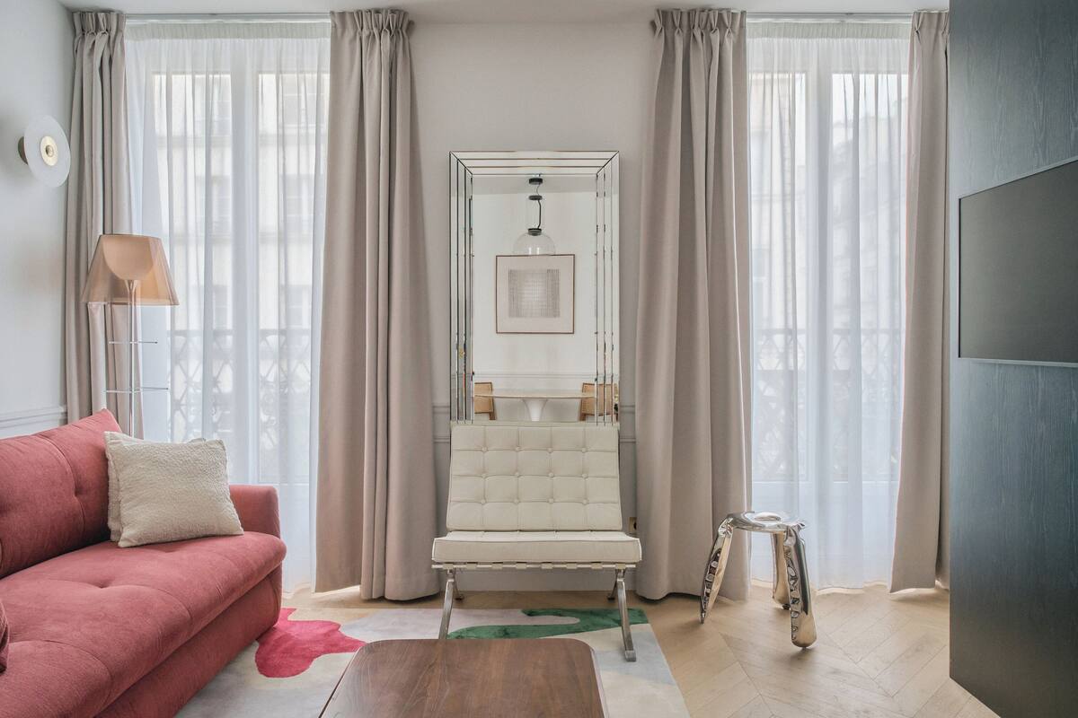 A modern living room with a pink sofa, a white armchair, a small side table, and a floor lamp.