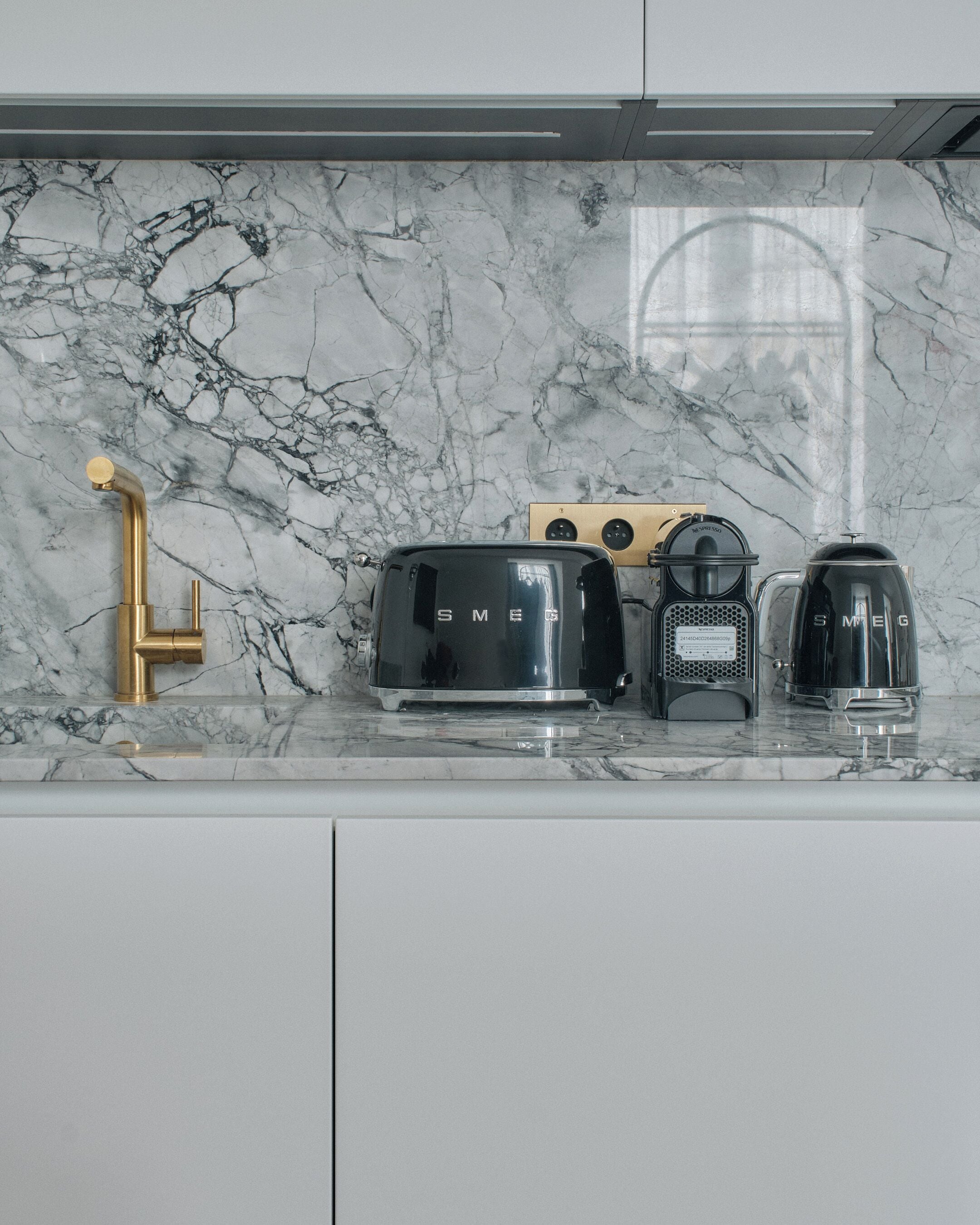 A kitchen with a marble countertop, a gold faucet, a black toaster, a coffee maker, and a kettle.