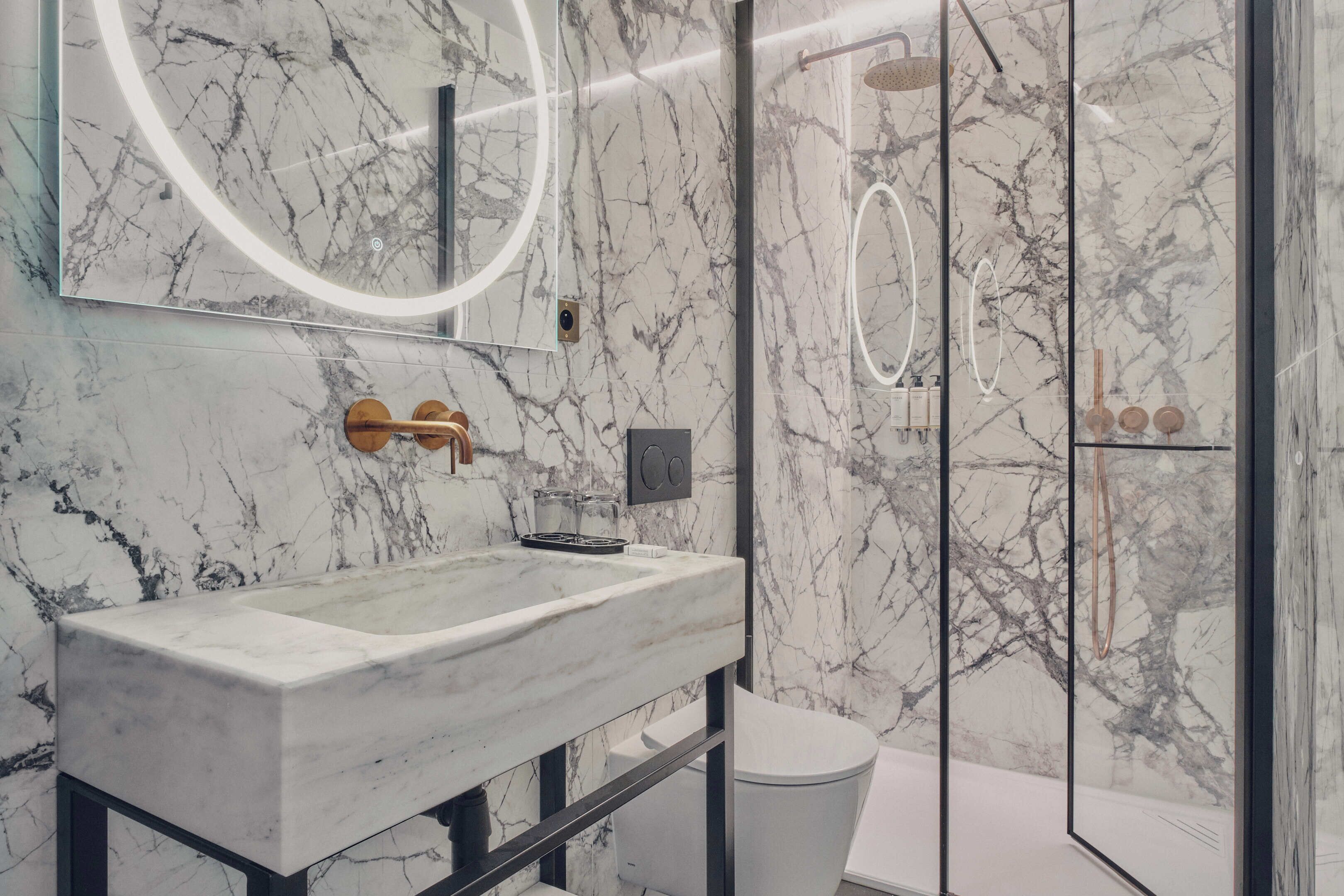 A modern bathroom with a marble sink, a large mirror, and a glass-enclosed shower area.