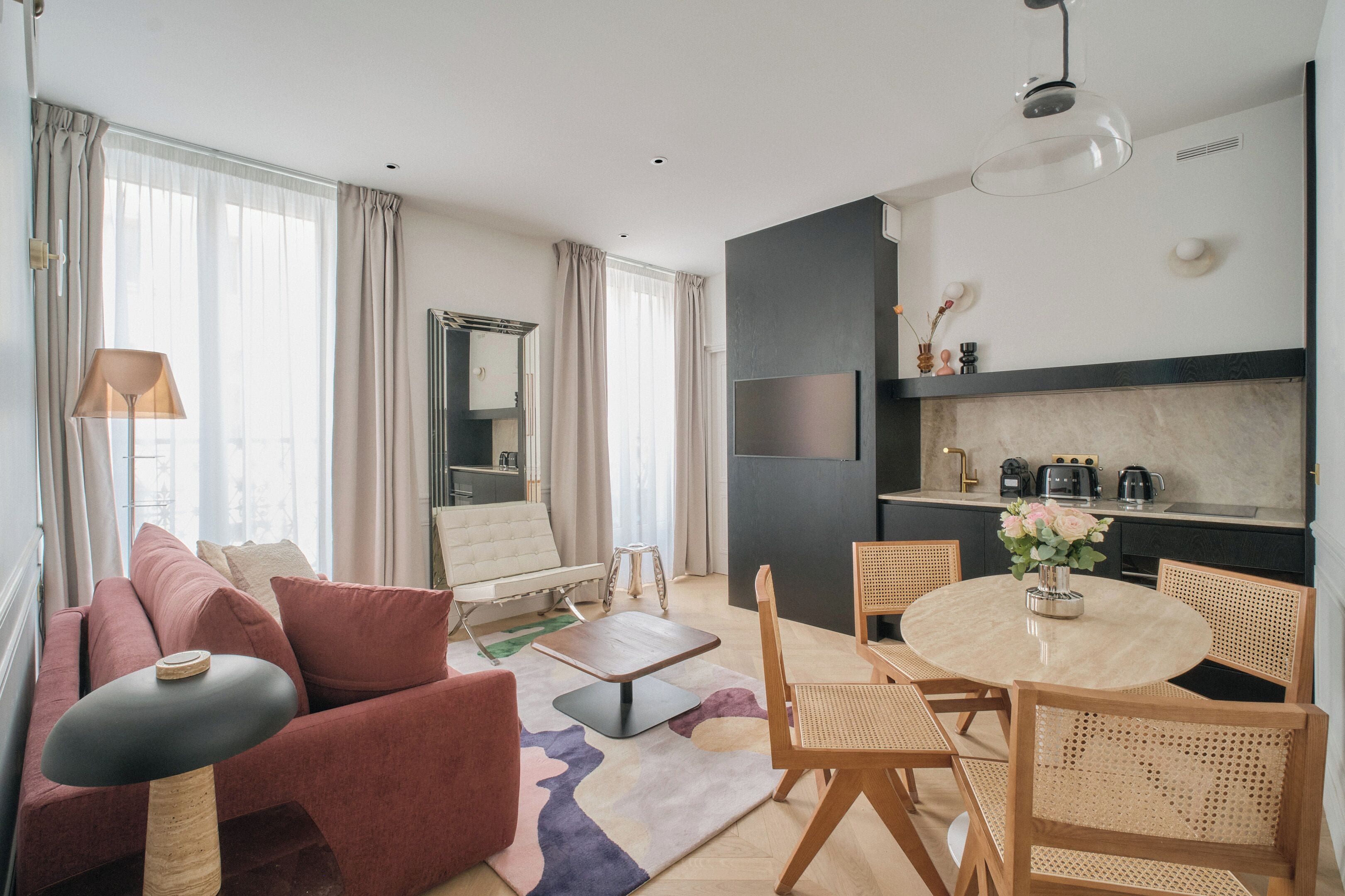 Un salon moderne comprenant un canapé, une table basse et un coin repas avec des chaises. Il y a également une cuisine équipée d’un téléviseur et d’appareils électroménagers.