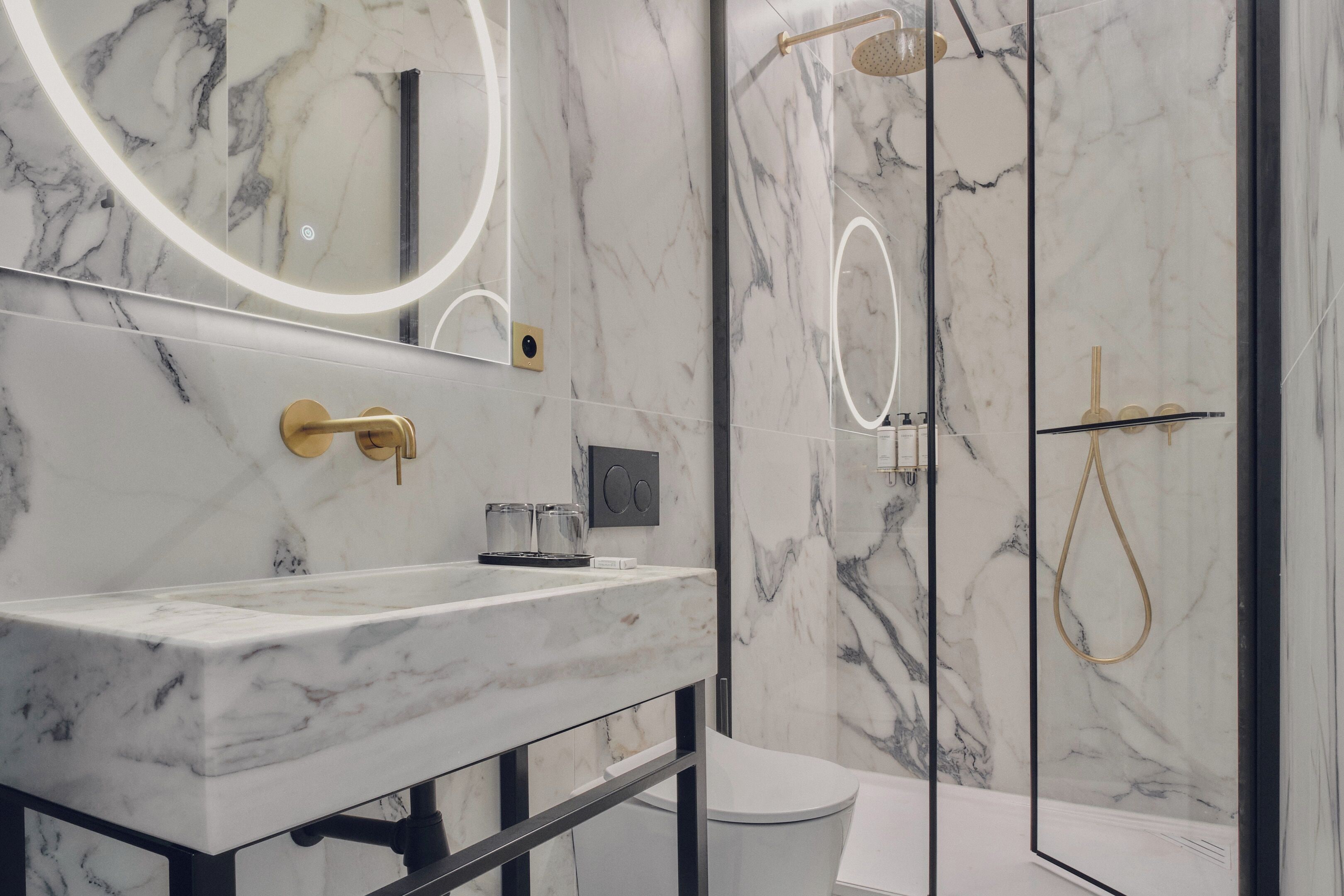 Een moderne badkamer met een marmeren wastafel, gouden details en een douche met glazen wanden.