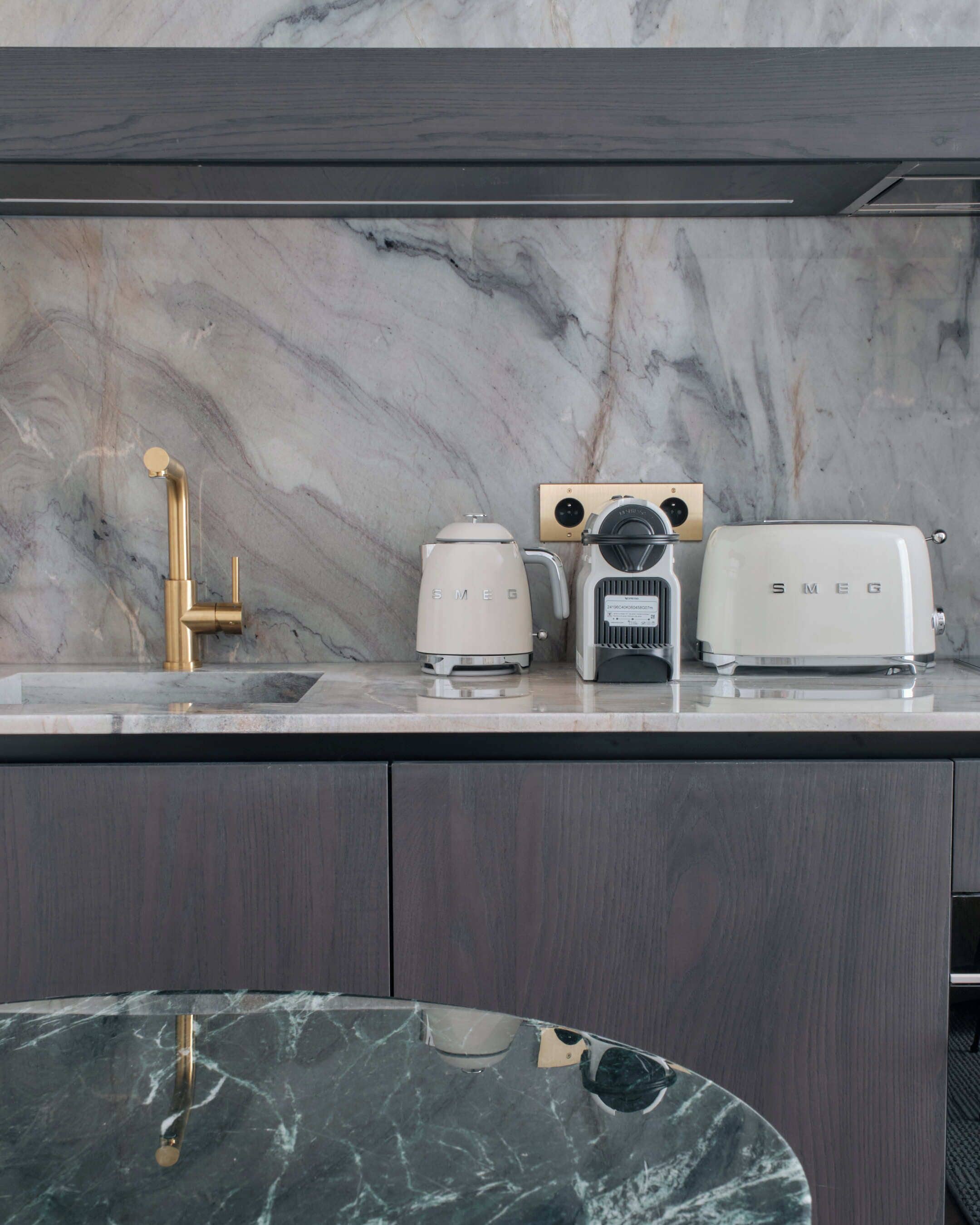 A kitchen with a marble countertop, a gold faucet, a coffee maker, a toaster, and a microwave.