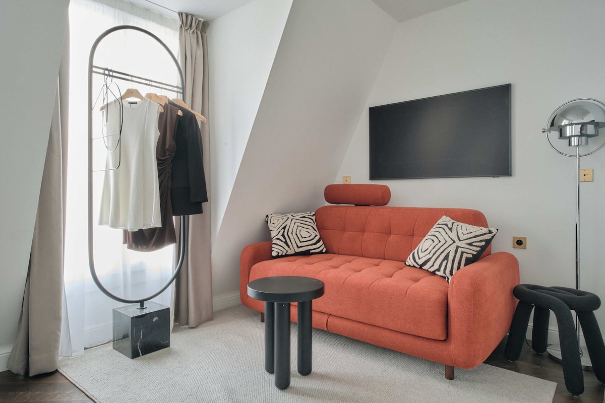 A modern room with a sofa, a round table, a mirror, and a hanging light fixture.