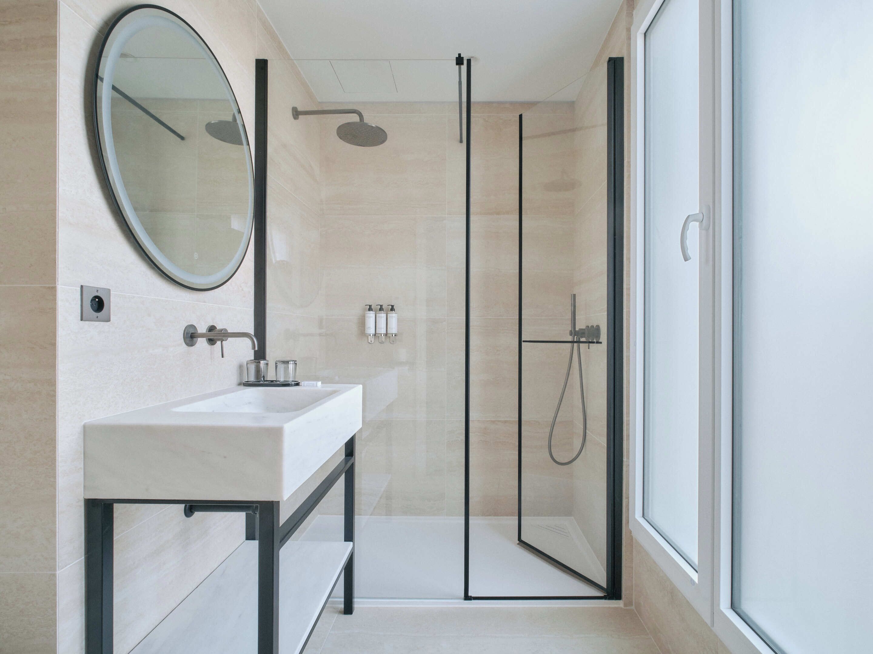 A modern bathroom with a glass-enclosed shower, a large mirror, and a white sink.