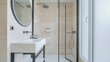 A modern bathroom with a glass-enclosed shower, a large mirror, and a white sink.