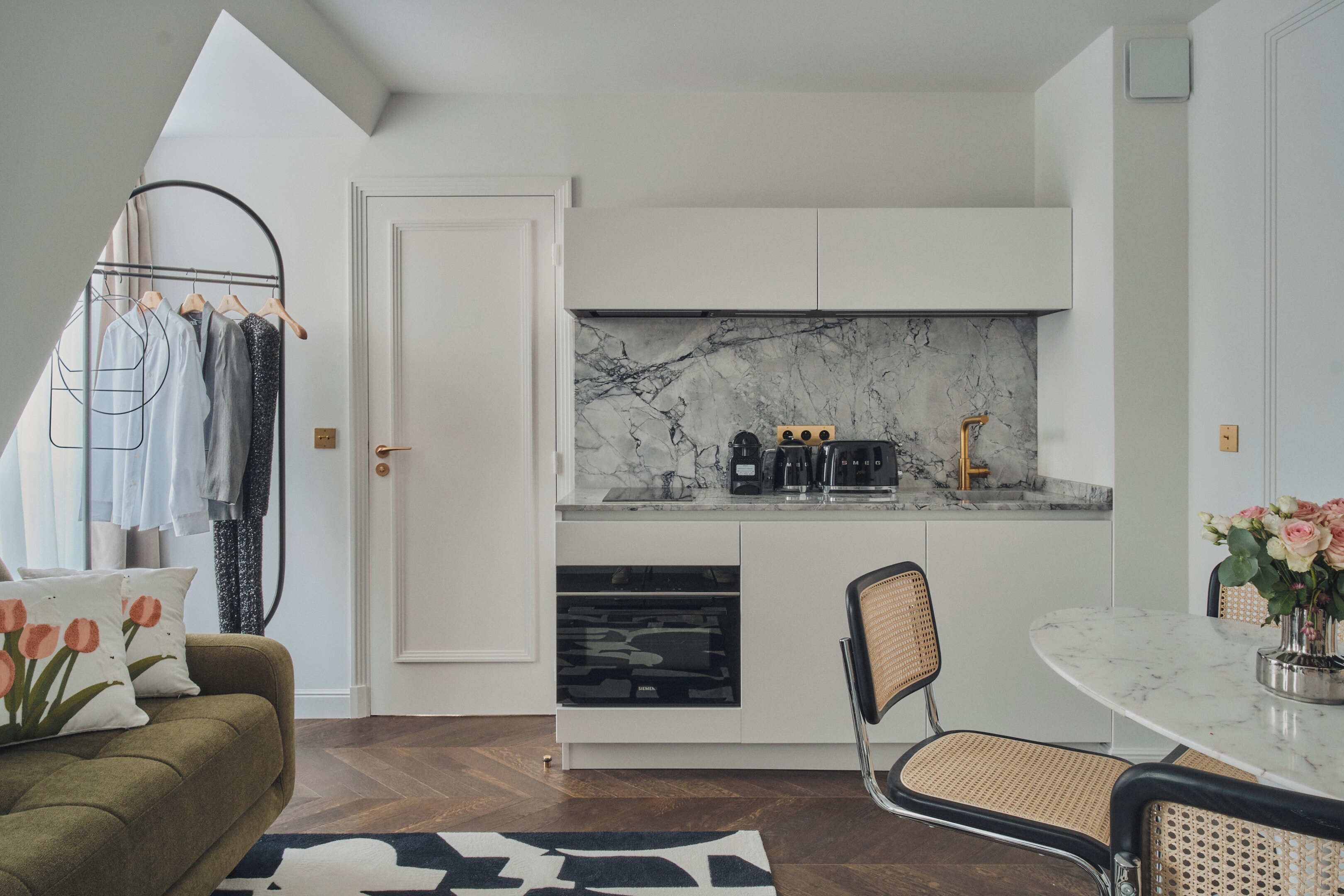 A compact kitchen with white cabinets, a marble backsplash, and a coffee maker.