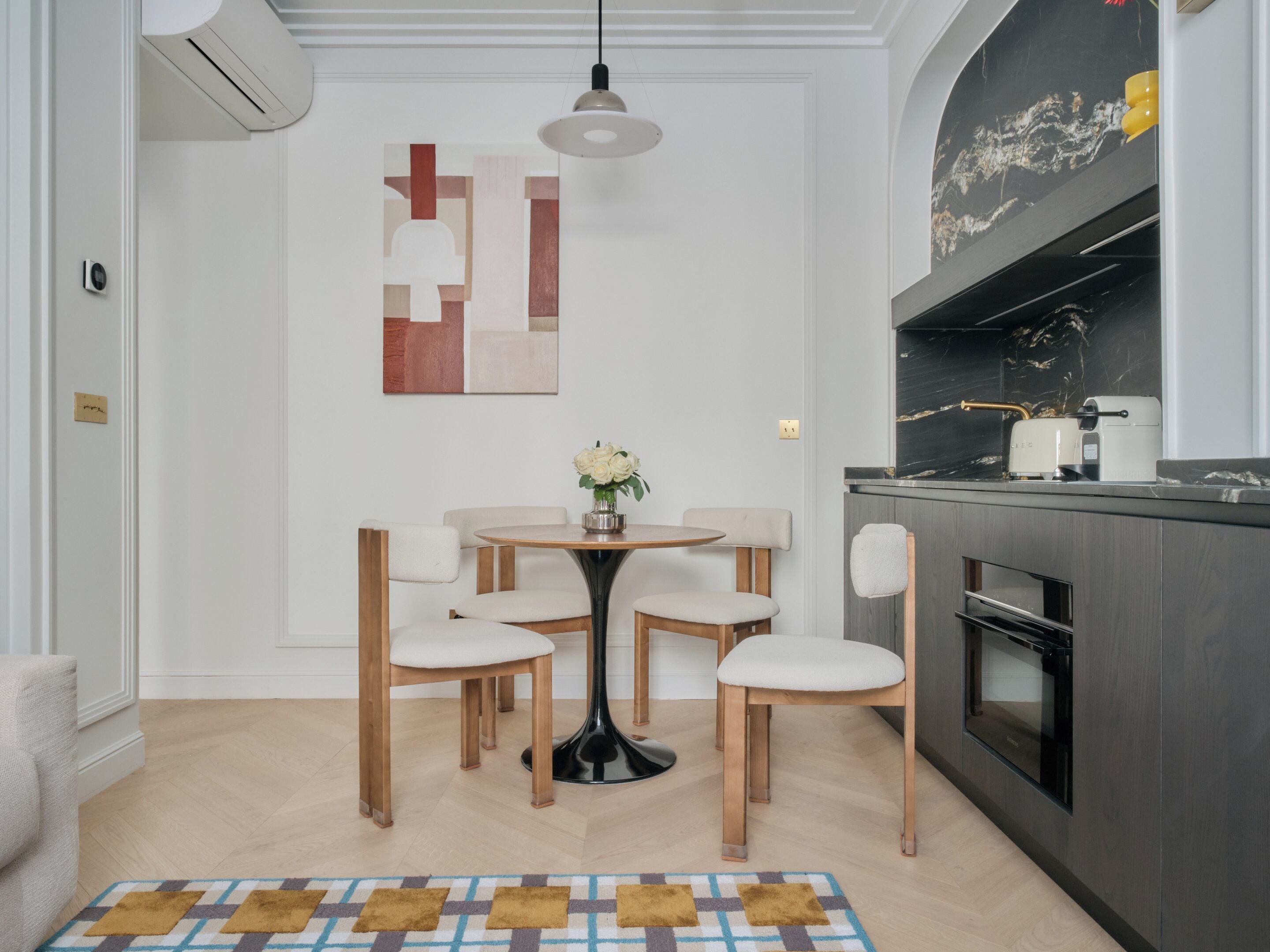 A modern kitchen with a dining area, featuring a round table with chairs, a hanging light fixture, and a marble backsplash.