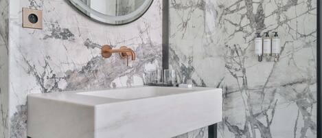 A bathroom with a marble backsplash, a round mirror, a white sink, and black metal frames.
