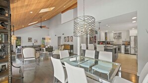 Une cuisine spacieuse équipée d’appareils électroménagers modernes, un coin repas avec une table en verre et un ventilateur de plafond.