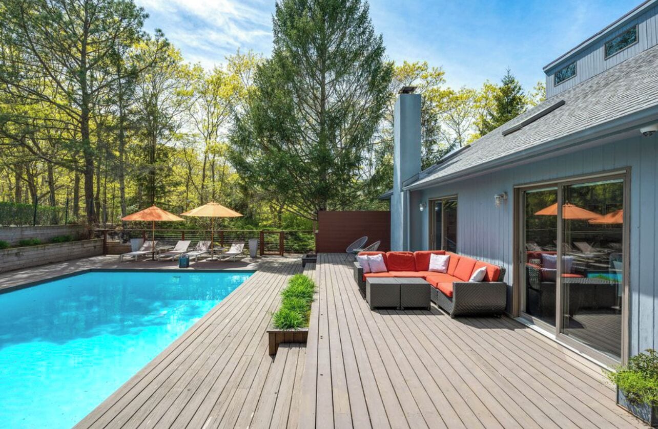 A modern house with a wooden deck, a swimming pool, and outdoor seating.