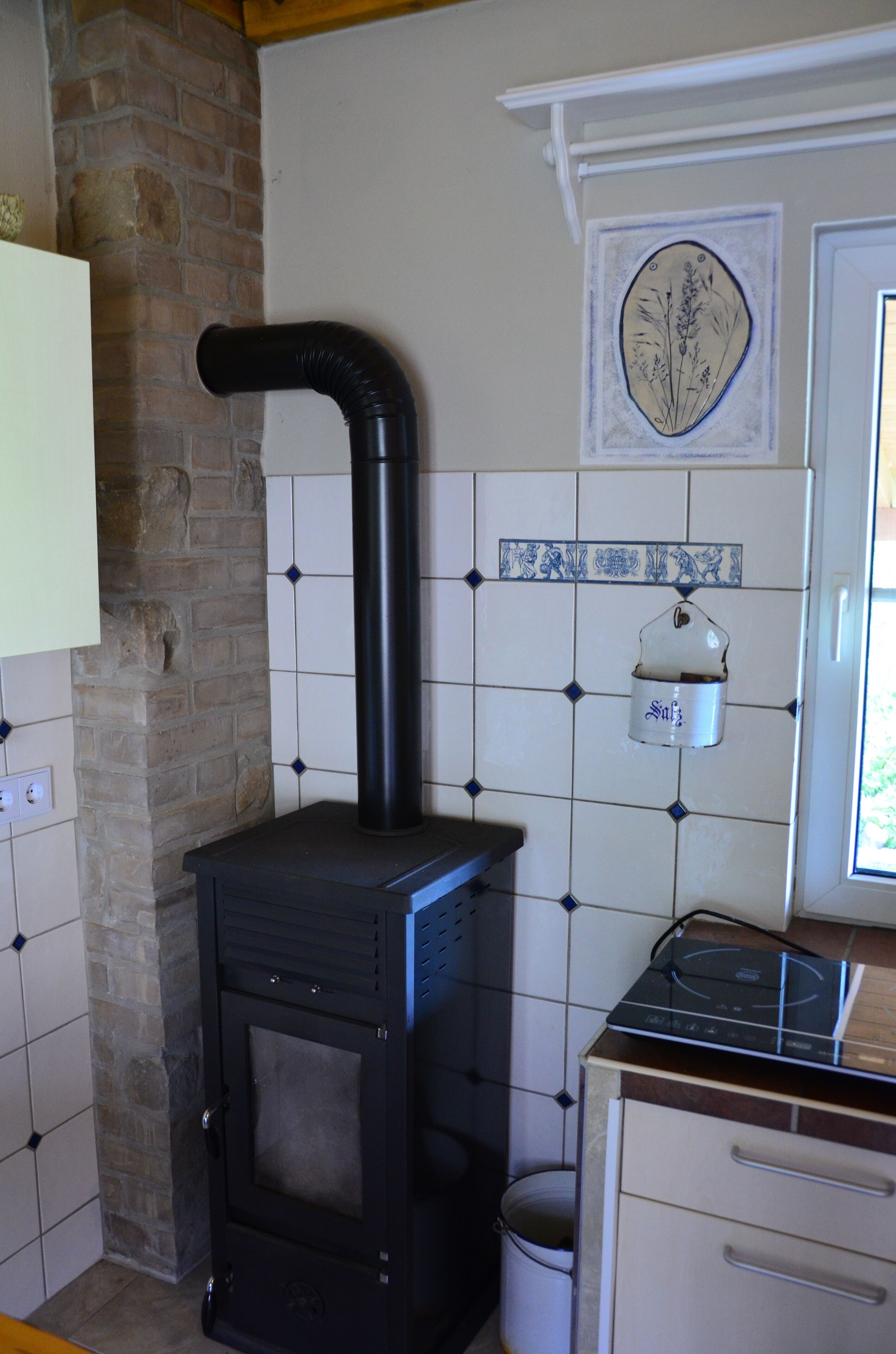 A kitchen with a black stove, white tiled walls, a brick wall, and a white cabinet.
