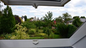A view from a window with a skylight, overlooking a well-maintained garden with various plants and a lawn. - Blüten Remise - Welcome to the flower city of Werder! (Werder (Havel))
