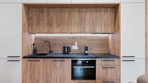 A compact kitchen with wooden cabinets, a black sink, a kettle, and a built-in oven. - Javorná Lodge by Interhome (Javorná)