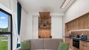 A modern kitchen with wooden cabinets, a dining area with a table and chairs, and a large window with curtains. - Javorná Lodge by Interhome (Javorná)