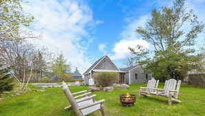 A house with a grassy yard, a fire pit, and Adirondack chairs. - Sand Cove Cottage-New! (Gouldsboro)